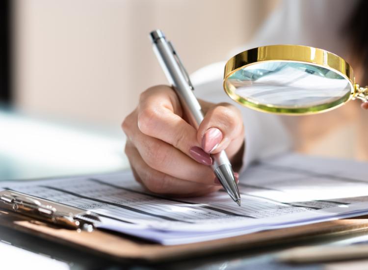 Photo of a womans hand holding a magnifyer over a writing pad.