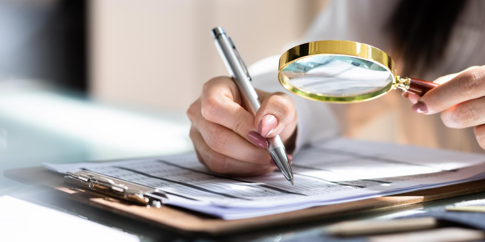 Photo of a womans hand holding a magnifyer over a writing pad.